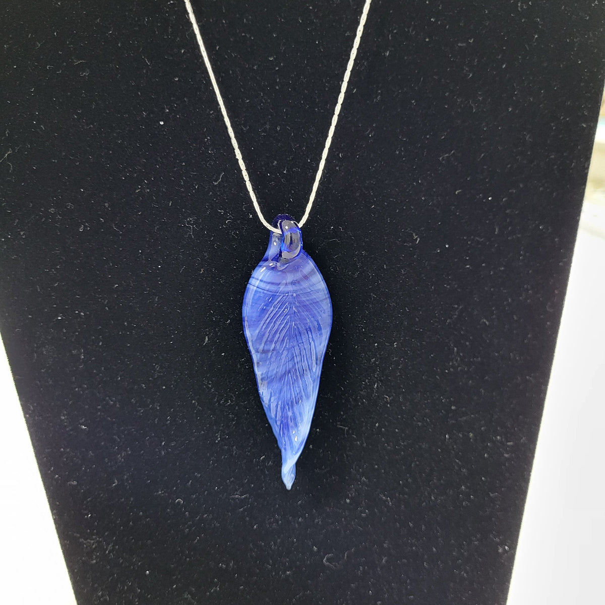 A blue glass pendant necklace with a silver chain, displayed on a black jewelry bust.