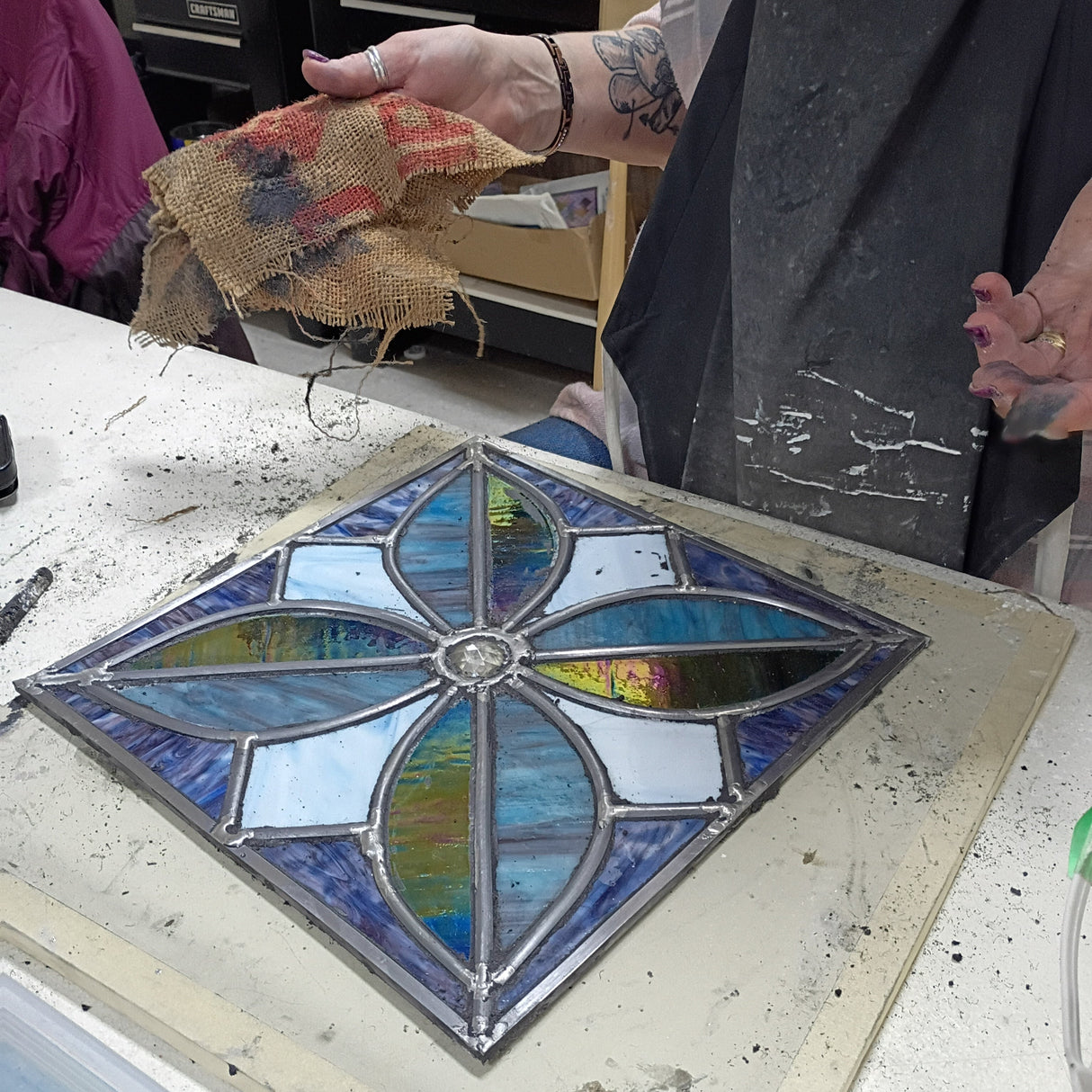 Stained glass panel on a table with a person's hand and arm in the foreground.