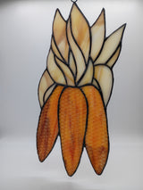 A stained glass window panel depicting a cluster of ears of corn, featuring cream and light tan glass sections for the husks and orange-brown glass sections for the kernels, outlined with dark metal solder lines.