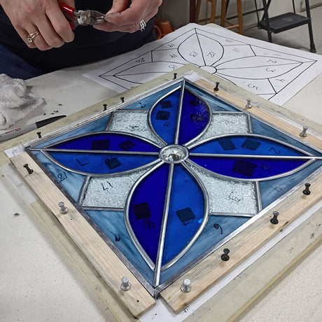 Stained glass panel with blue and clear design in a wooden frame, being worked on.