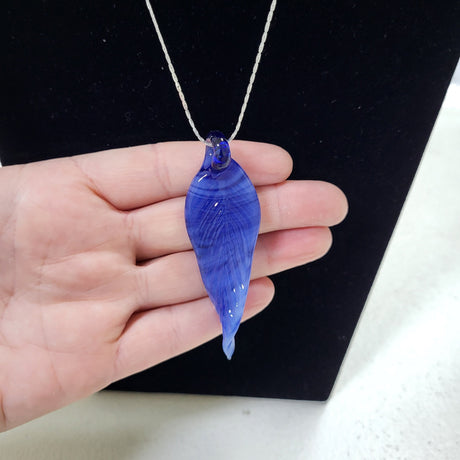A hand holding a blue teardrop-shaped pendant necklace on a silver chain against a black display background.