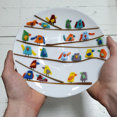 hands holding white fused glass plate with multicolored birds