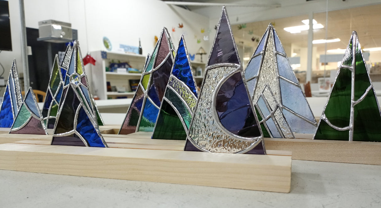 Stained glass mountain and moon designs on a wooden base in a workshop setting.