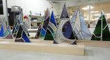 Stained glass mountain and moon designs on a wooden base in a workshop setting.