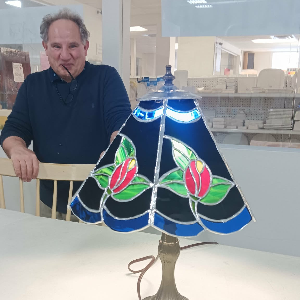 Man standing next to a stained glass lamp with floral design in a room setting.