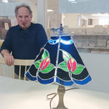 Man standing next to a stained glass lamp with floral design in a room setting.